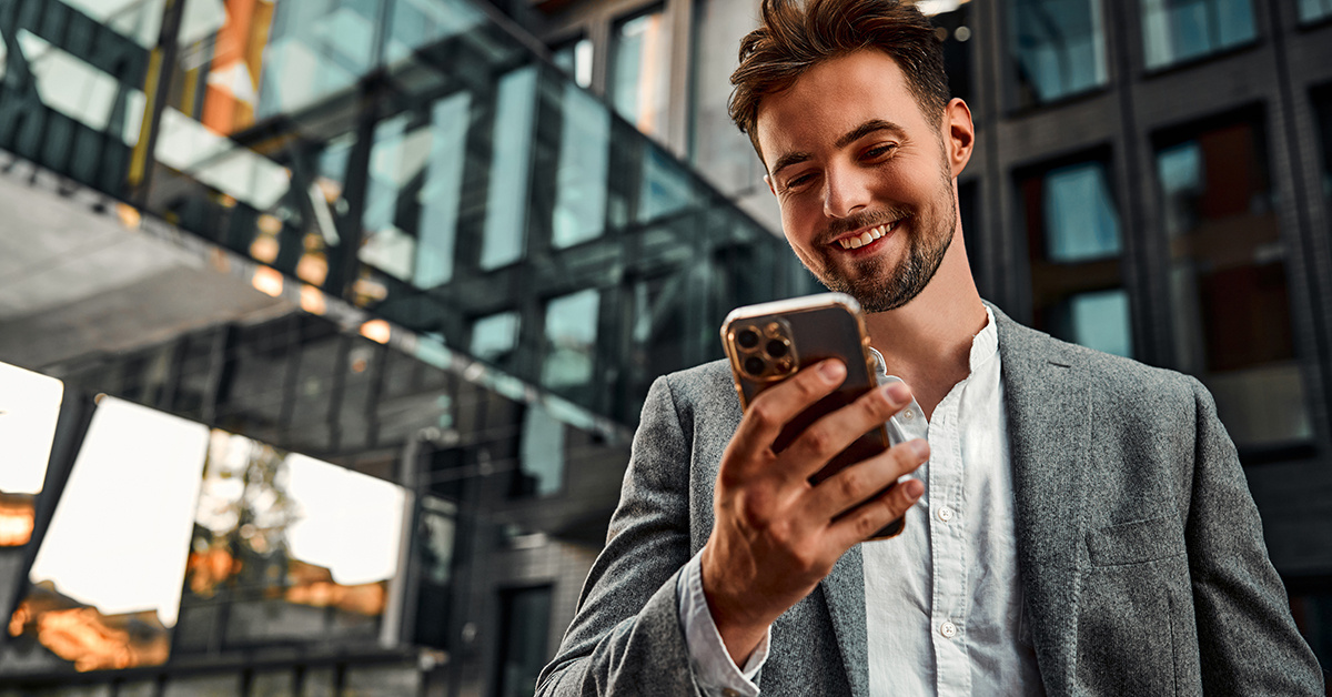 Business-Mann schaut von unterwegs auf sein Smartphone. Und freut sich, wie einfach er von Unterwegs aus Arbeiten kann.